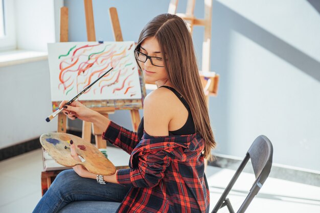 Fille peintre pensif créatif peint une image colorée sur toile avec des couleurs à l'huile en atelier.