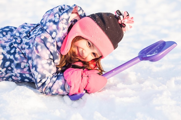 Fille avec une pelle allongée sur la neige