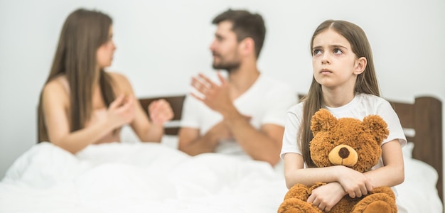 La fille avec une peluche assise près des parents dans le lit