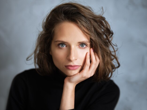 fille pensive aux cheveux bouclés en bataille, elle pense à quelque chose et touche le menton