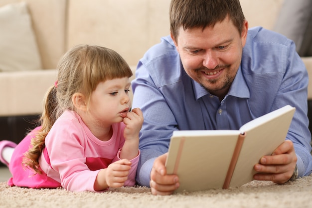 Fille père lecture livre allongé sur un tapis