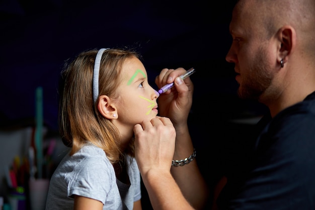 Fille et père peignent un visage, s'amusent, s'amusent ensemble à la maison sur le canapé