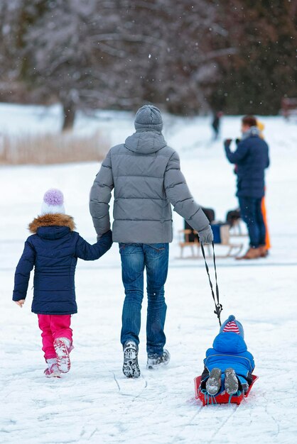 Fille avec père tirant un traîneau avec son fils sur la patinoire d'hiver. La luge est une activité, généralement pratiquée en position couchée ou assise sur véhicule. L'utilisation pratique des traîneaux est ancienne et répandue