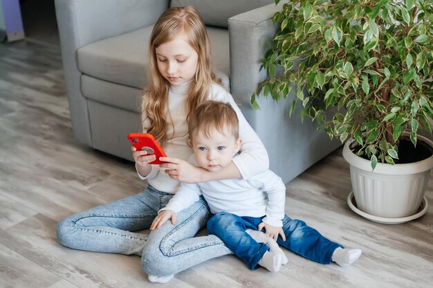 Une fille avec un petit frère assis sur le sol avec un smartphone