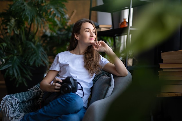 Une fille photographe avec un appareil photo sourit assis sur une chaise avec de nombreux livres