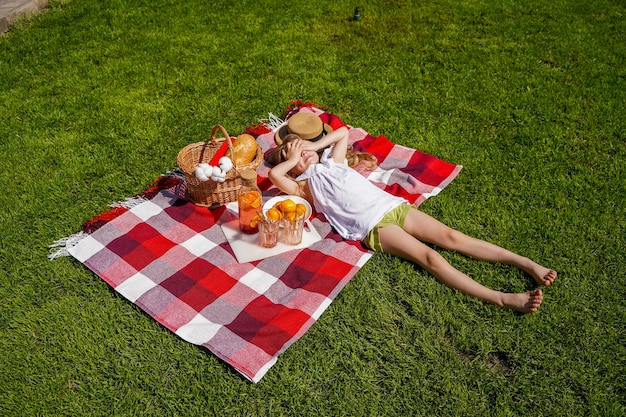 Une fille en pique-nique sur l'herbe une couverture à carreaux rouge un panier en osier une boisson naturelle à base d'oranges ...