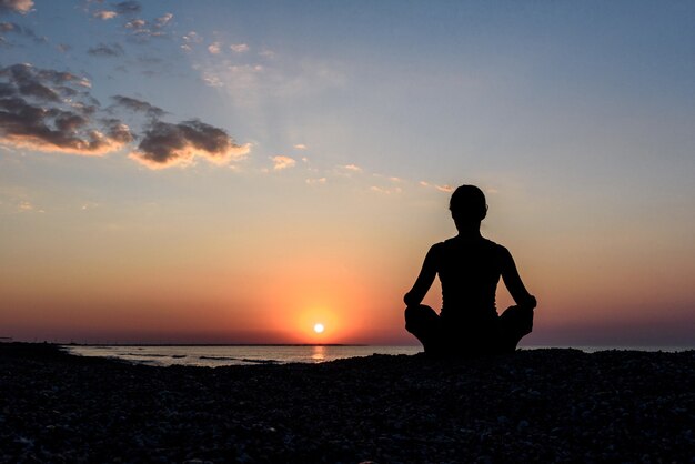 Fille sur la plage à l'aube en yoga assana, silhouette