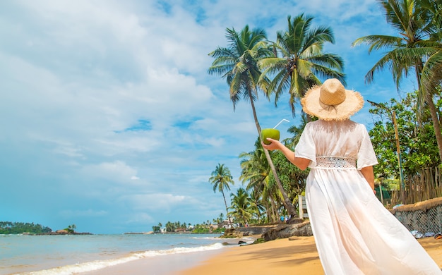 Fille sur la plage boit de la noix de coco.