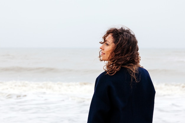 Fille pluie mer vent hiver portrait femme sourire printemps manteau cheveux longs bouclés humeur rive neige plage