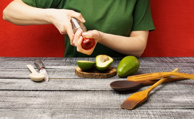 La fille poivre un avocat. Jeune femme à l'avocat frais à la table. Le processus de préparation d'aliments sains.