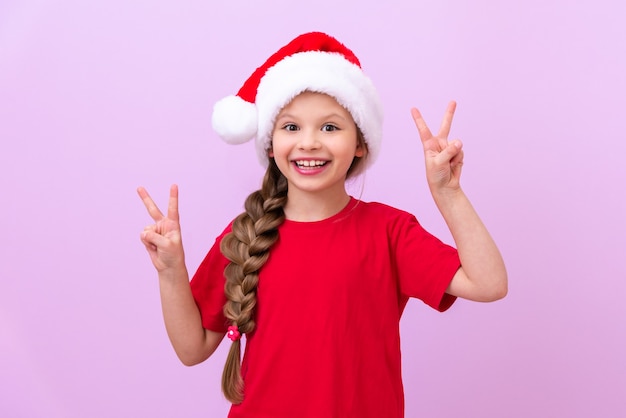 Une fille portant un chapeau du Nouvel An et un T-shirt rouge montre ses doigts sur ses mains.