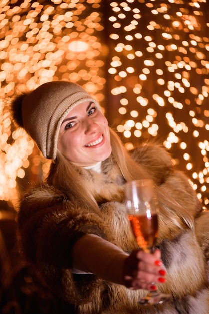 Fille portant un chapeau d'hiver élégant avec une coupe de champagne à la fête sur fond d'or brillant de vacances.