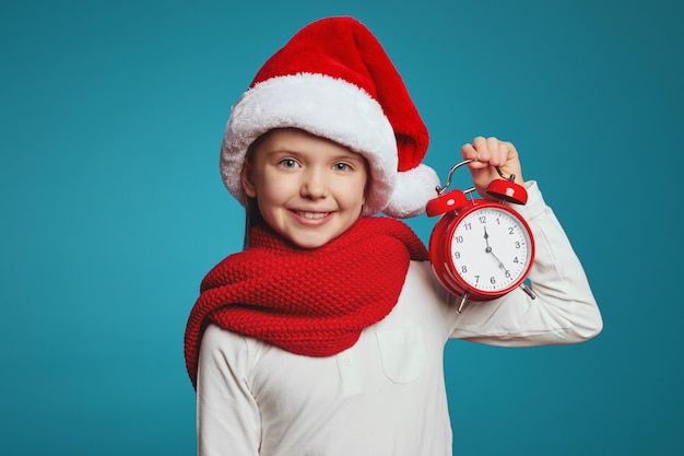 Fille portant un chapeau de Noël et une écharpe rouge tenant un réveil isolé sur