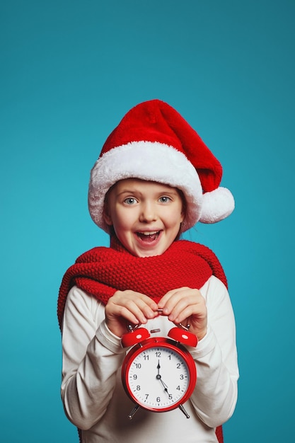 Fille portant un chapeau de Noël et une écharpe rouge tenant un réveil isolé sur