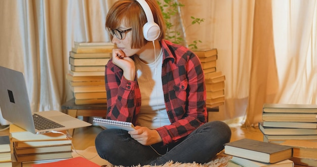 une fille portant des écouteurs est assise sur un tapis et lit un livre