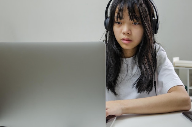 Fille portant des écouteurs étudiant en ligne avec un ordinateur portable et écoutant de la musique relaxante ou jouant aux médias sociaux sur Internet à la maison