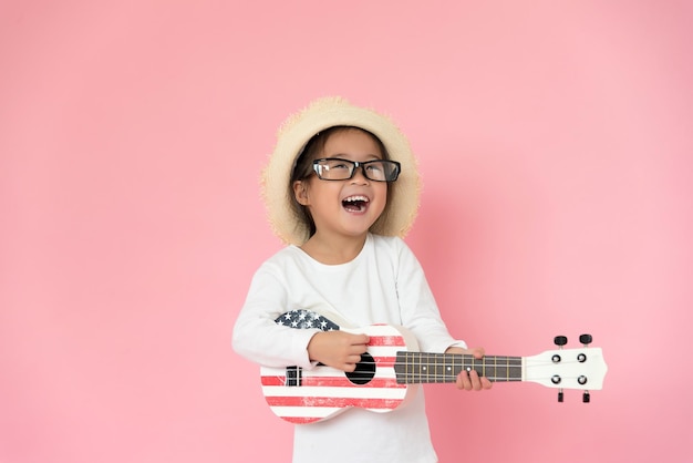 Une fille portant des lunettes et un chapeau en jouant de la guitare sur un fond rose