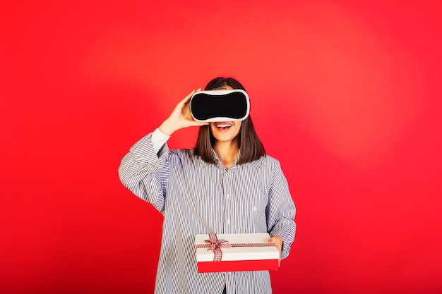 Fille portant des lunettes de réalité virtuelle VR tenant une boîte-cadeau sur le fond rouge.
