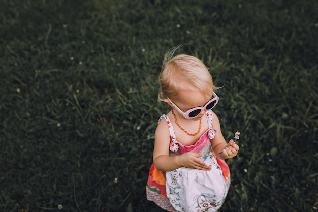 Fille portant des lunettes de soleil tout en tenant une fleur sur l'herbe