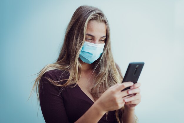 Une fille portant un masque en raison d'un coronavirus regarde son téléphone