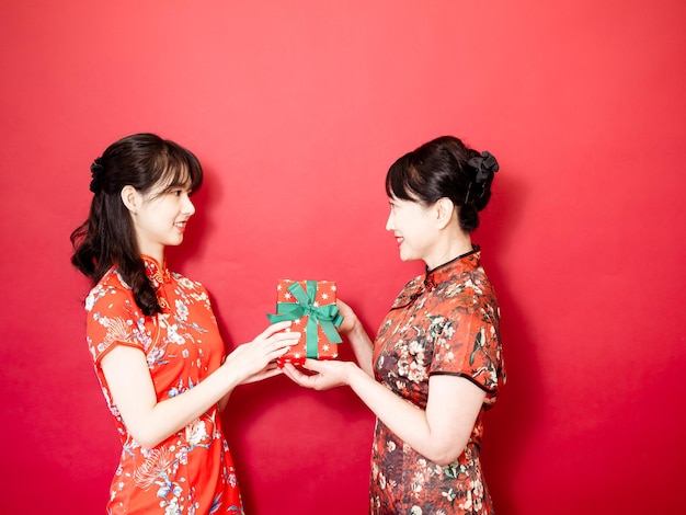 Fille portant le qipao cheongsam traditionnel félicite maman et offre un cadeau emballé dans une boîte cadeau Vacances en famille et convivialité