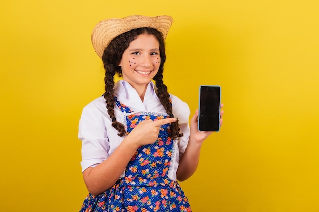 Fille portant des vêtements typiques pour Festa Junina pointant vers la technologie des applications mobiles Pour la fête d'Arraia