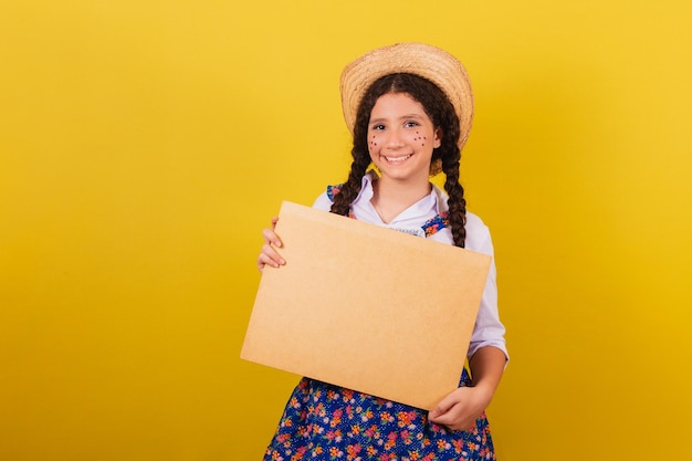 Fille portant des vêtements typiques pour Festa Junina tenant un écran pour le texte ou l'annonce Pour la fête d'Arraia