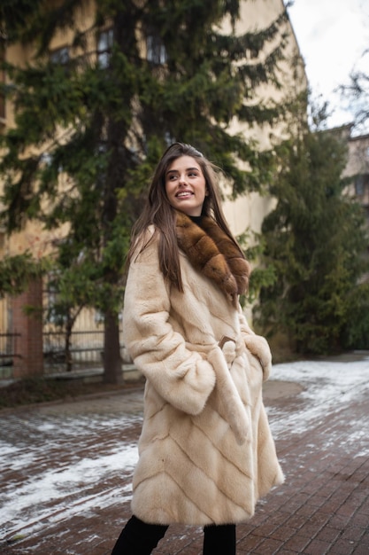 Fille posant sur la route sur fond d'hiver Glamour drôle jeune femme avec sourire portant élégant manteau de fourrure long gris Fourrure et concept de mode Belles personnes