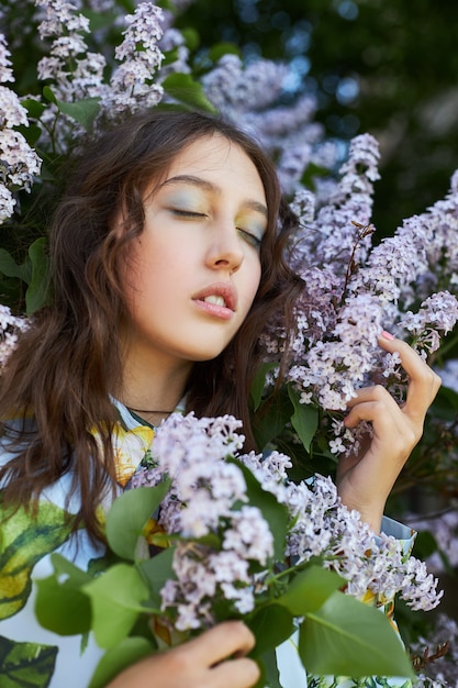 Fille pose dans un buisson de lilas au printemps. Portrait romantique d'un enfant en fleurs à la lumière du soleil