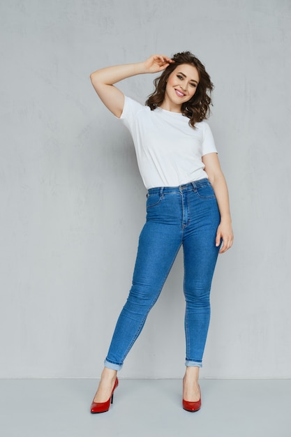 Fille positive en jeans, t-shirt blanc et talons aiguilles rouges posant