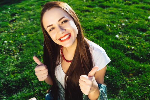 Fille positive montre les pouces vers le haut. Étudiant heureux dans le parc