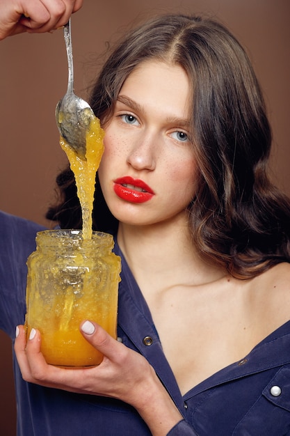 Fille avec pot de miel. Concept d'alimentation saine, régime alimentaire, dessert. belle fille tient une cuillère en argent avec du miel