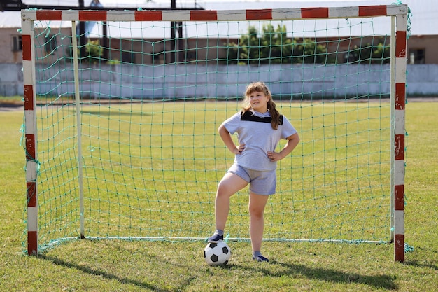 Une fille potelée en vêtements de sport se tient dans la porte du football et appuie sur la balle avec son pied