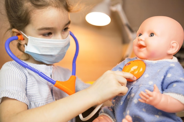 Une fille avec une poupée joue au docteur, une infirmière écoute le bébé à travers un stéthoscope. Pédiatrie, calendrier de vaccination, jeu de profession. Examen médical