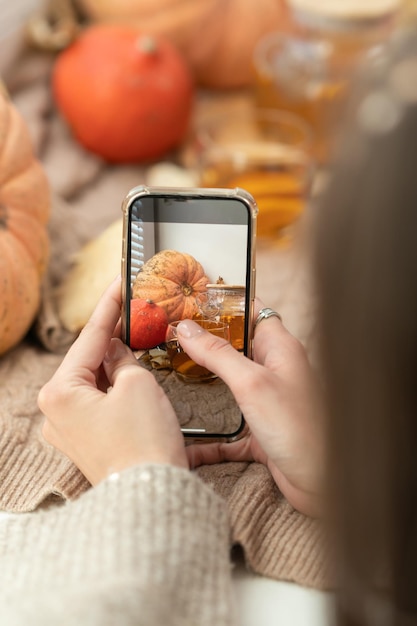 Fille prenant une photo de feuilles d'automne de citrouilles et d'une théière sur une fenêtre Fille photographiant au téléphone composition d'halloween rustique Joyeux Thanksgiving et Halloween