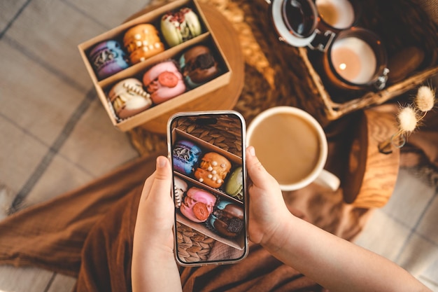 Photo fille prenant une photo de haut en bas d'une boîte de macarons avec divers assortiments à l'aide de son téléphone