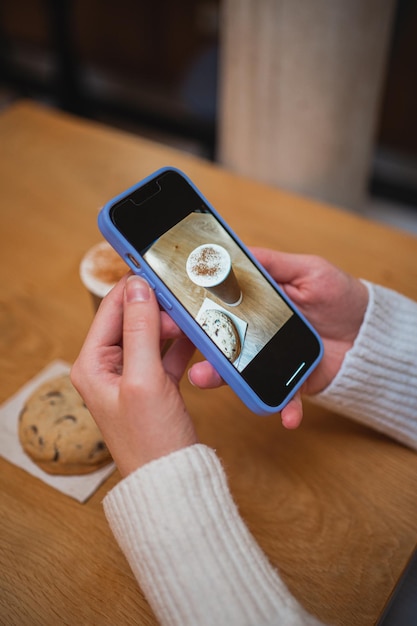 Fille prenant une photo de son café et biscuit avec son téléphone intelligent pour les médias sociaux Elle est dans un café
