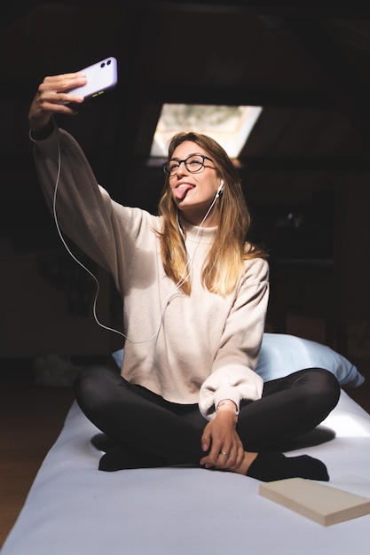 Photo fille prenant un selfie avec sa langue dans son lit