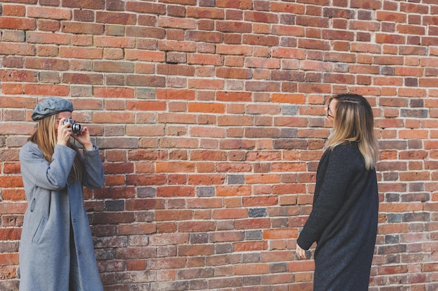 Une fille prend une photo de son amie devant un mur de briques dans un espace de copie de rue urbaine et un photographe de lieu vide et un concept de mode de vie urbain pour les jeunes