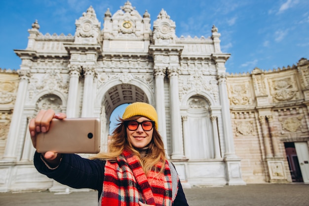 Fille prend un selfie sur la place en face de Dolmabahce, Istanbul, Turquie. Une jeune fille touriste dans un chapeau et un manteau est photographiée au téléphone devant le Palais du Sultan à Istanbul.