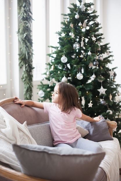 Fille près de l'arbre de Noël, attendant le père Noël et un miracle