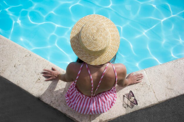 fille près de la piscine dans un chapeau de paille en été