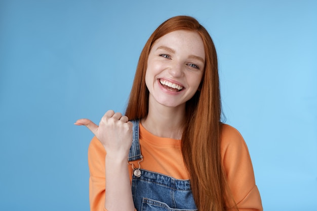 Fille présentant son amie pointant le pouce vers la gauche souriante riant joyeusement en disant fièrement aux pros un produit cool recommande de parler d'un café confortable et savoureux qui s'amuse en posant un fond bleu.