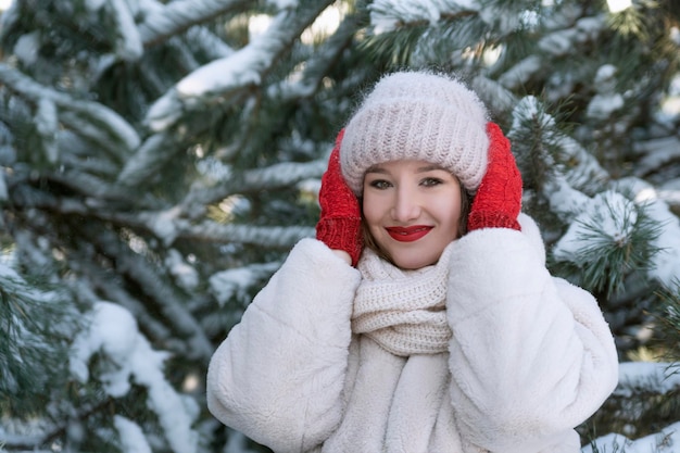 Fille profite d'une journée d'hiver glaciale dans le parc Portrait de jeune femme sur fond de pins enneigés