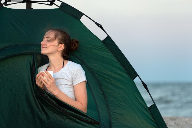 Fille profite de la matinée dans une tente au bord de la mer Tasse de thé dans les mains Voyage randonnée camping