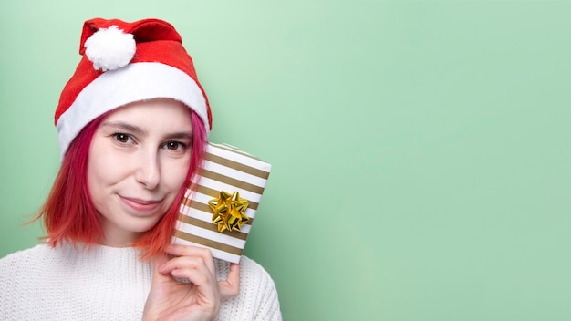 Fille en pull blanc et bonnet de Noel, tient le cadeau en main sur le vert