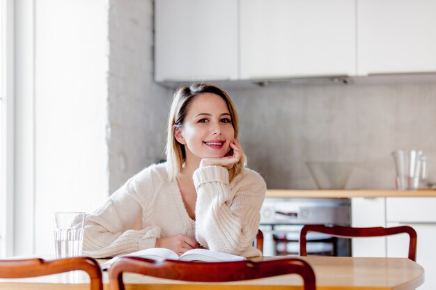 Fille en pull blanc avec livre assis à table