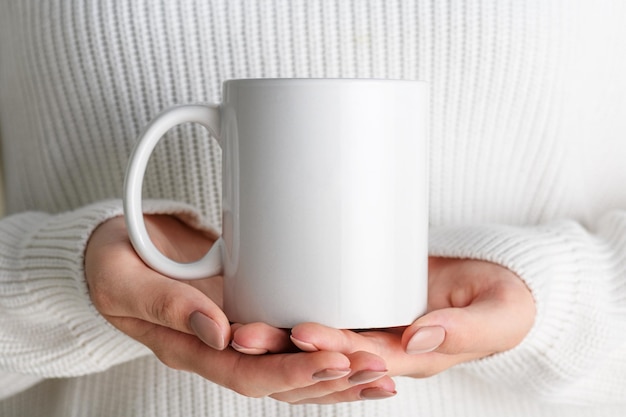 Fille en pull blanc tenant une tasse de café en porcelaine blanche maquette gros plan