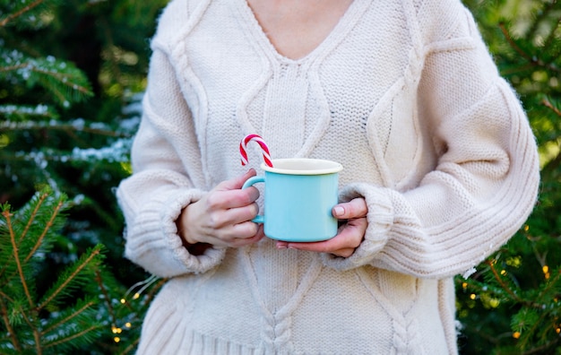 Fille en pull blanc tenant une tasse de café près de sapin