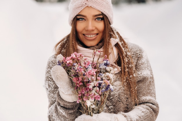 Une fille en pull en hiver avec un bouquet dans les mains se dresse parmi de grandes congères.